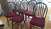 Full view of all six dark oak Windsor bow back chairs arranged together showing burgundy foam cushions.