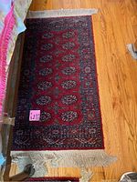 Smaller of the two rugs showing detailed pattern and fringes, placed on wooden floor.