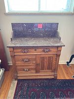 Front view of antique oak dresser with dark marble top and backsplash, three drawers with wooden knobs, and a cabinet door beneath.