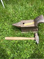Anvil and sledgehammer resting on grass for size and detail view