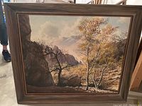 Large framed painting showing rocky mountain terrain with a tree with autumn leaves in foreground