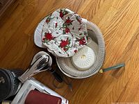 Photo of handheld hair dryer, fabric hair dryer hood with floral pattern, hose, and round plastic diffuser bowl on a wood floor.