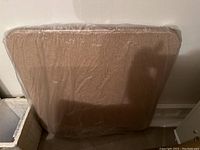 Photo of card table wrapped in plastic cover in basement against wall.