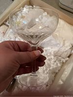 Hand holding a short-stem crystal glass with an etched floral or fruit pattern on the bowl.