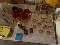 Top-down view of the lot showing copper mugs, tall frosted decorated glasses, small clear glasses with gold bases, black shot glasses, and part of the metal serving tray.