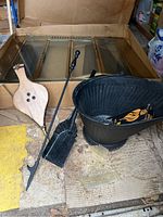 Photo showing the fireplace glass doors with metal frame, black metal grate, black metal bucket, fireplace poker and shovel tools, and wooden bellows in foreground.