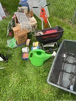 Lot taken outside on grass showing various gardening supplies including seed spreader, watering can, planters, fencing, and box with tools.