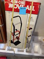 Original box of 4-in-1 All in One Hand Dolly with black and red dolly image on front, elastic bands securing box with lot sticker number.