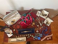 Full overview of jewelry and watches laid out on a wooden table including bracelets, earrings, necklaces, and pins.