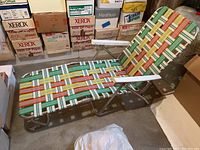Lawn recliner chair with multicolored webbing and aluminum frame in storage area with boxes around