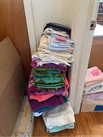 Stack of multi-colored kitchen towels and linens piled in vertical stacks by a wall corner