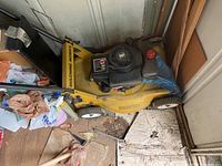 Photo of yellow mulching mower with black gas engine stored indoors on wood floor