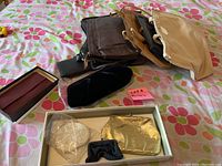 Overview of the purses and wallets arranged on a floral bedspread with a pink sticky note marked 'lot 9'. Items include four fabric or leather purses in beige, brown, and black, two gold-tone metallic evening purses in a box, one small black velvet clutch purse, and one small wallet or card holder.