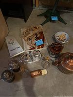 Overview of miscellaneous kitchen items including silver-plated containers, copper teapot, pepper grinder, braided cords, and ceramic bowl with wooden pieces.