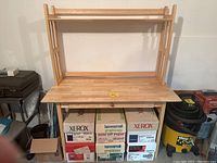 Wooden table with an attached hutch, light wood color, with boxes placed underneath the table surface. Hutch has open shelves and vertical slats on the sides. Needs cleaning according to seller.