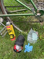 Close-up of Snap Fix-A-Flat tire sealant can, coiled cable lock, blue glove, and plastic jug shown on grass near bicycle wheel.