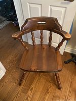 Close-up front view of one wooden captain's chair highlighting curved backrest, spindles, armrests and seat.