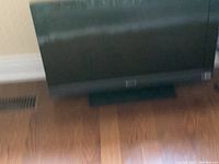 Photo of a black flat screen TV approximately 32 inches in size, set on a stand on a wooden floor.