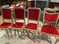 Four antique chairs with red upholstery and decorative nailhead trim, showing detailed claw-foot legs on front.