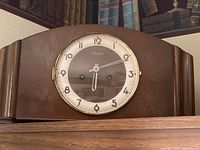 Wooden antique mantel clock showing round clock face with glass cover and Arabic numerals