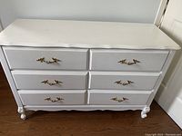 Front view of the white long dresser with six drawers and gold-tone handles, showing carved legs and detailed edges.