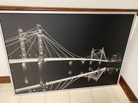 Overall view of the framed black and white picture showing the illuminated Albert Bridge at night with reflections in water.
