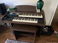 Front view of a wooden electronic organ with two keyboards and control panel, sitting on matching wooden bench.