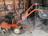 Side view of an orange garden rototiller with a black engine, single wheel in front, and four metal tines. Attached black collection bag labeled 'Duro Bio-Force'.
