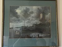Photo of framed landscape picture showing a harbor with a windmill under cloudy skies.
