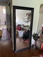 Full view of the large rectangular mirror with black frame leaning against wall in room, showing reflection of interior space.