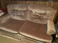 Brown velvet loveseat with tufted back cushions, rolled armrest on one side, and visible wear.