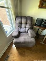 Photo of a brown reclining chair placed near a window and wooden floor with visible cushioning and fabric texture.