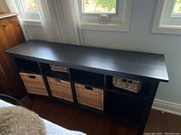 Front view of black IKEA sideboard, showing six lower compartments with three wicker baskets in some compartments.