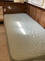 Photo of one twin bed with dark wooden headboard and light blue fitted sheet mattress.