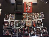 Photo showing an assortment of near mint NBA basketball cards arranged around a metal collector's tin box featuring a caricature of a player on the lid.