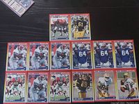 Top-down photo showing 15 NFL rookie trading cards from 1990 featuring different players in football action poses. Cards are laid out neatly on a black surface.