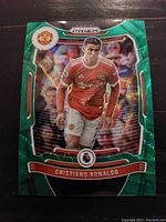 Close-up photo of green Panini Prizm Premier League card featuring Cristiano Ronaldo in Manchester United kit, showing holographic reflective finish and team and league logos.