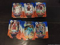 Photo showing several stacks of Prizm Premier League trading cards spread on a dark surface with visible players and team logos on card fronts.