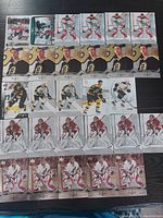 Photo showing 25 hockey cards laid out on a black surface. Cards include Boston Bruins players and Arizona Coyotes goalies from the Upper Deck Black Diamond series in near mint condition.