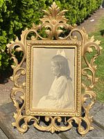 Front view of antique French solid bronze picture frame with ornate floral and scroll decoration holding a vintage sepia photograph of a young girl in profile.