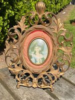 Front view of the antique bronze picture frame with visible ornate leaf and scroll design and central portrait.