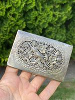 Front of silver card case showing pierced floral and bird design with raised details
