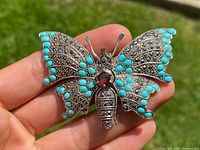 Front view of silver butterfly brooch showing turquoise cabochons, marcasite stones, and central red gemstone on wings and body