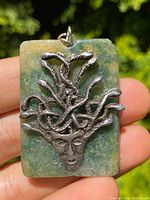 Front view of rectangular pendant showing silver Medusa head with snakes mounted on a green and yellowish stone background.