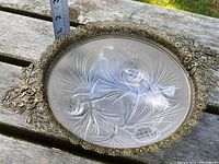 Top view of frosted glass bowl with pinecone and leaf designs, framed by ornate metal with leaf patterns and two handles.