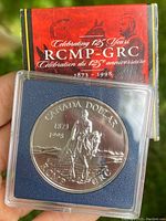 Obverse side of the coin showing mounted RCMP officer and commemorative inscriptions with packaging in background.