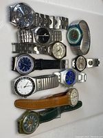 Photo showing 10 vintage Swatch wristwatches arranged on a white surface, featuring various dial colors and band types.