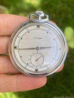 Front view of the CYMA pocket watch showing the silver Art Deco dial with black geometric hour markers and a small seconds subdial at the 6 o'clock position.