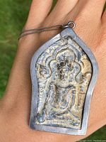 Front view of carved Buddha stone pendant set in a silver frame, displaying detailed Buddha figure and carved arch.