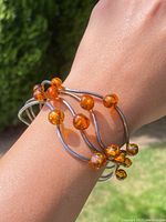 MCM cuff bracelet on wrist showing silver bands and multiple amber beads from top view
